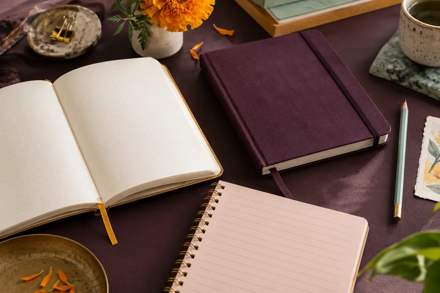 Three notebooks with different page layouts and bindings on a burgundy desk.